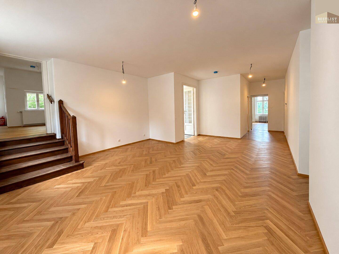 Großer, heller Raum mit Fischgrätparkettboden und einer eleganten Holztreppe, bereit zur individuellen Gestaltung.