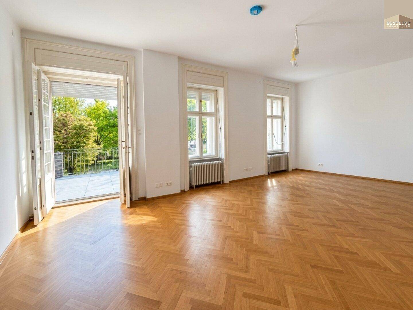 Heller Wohnraum mit Fischgrätparkett und direktem Zugang zu einer sonnigen Außenterrasse.