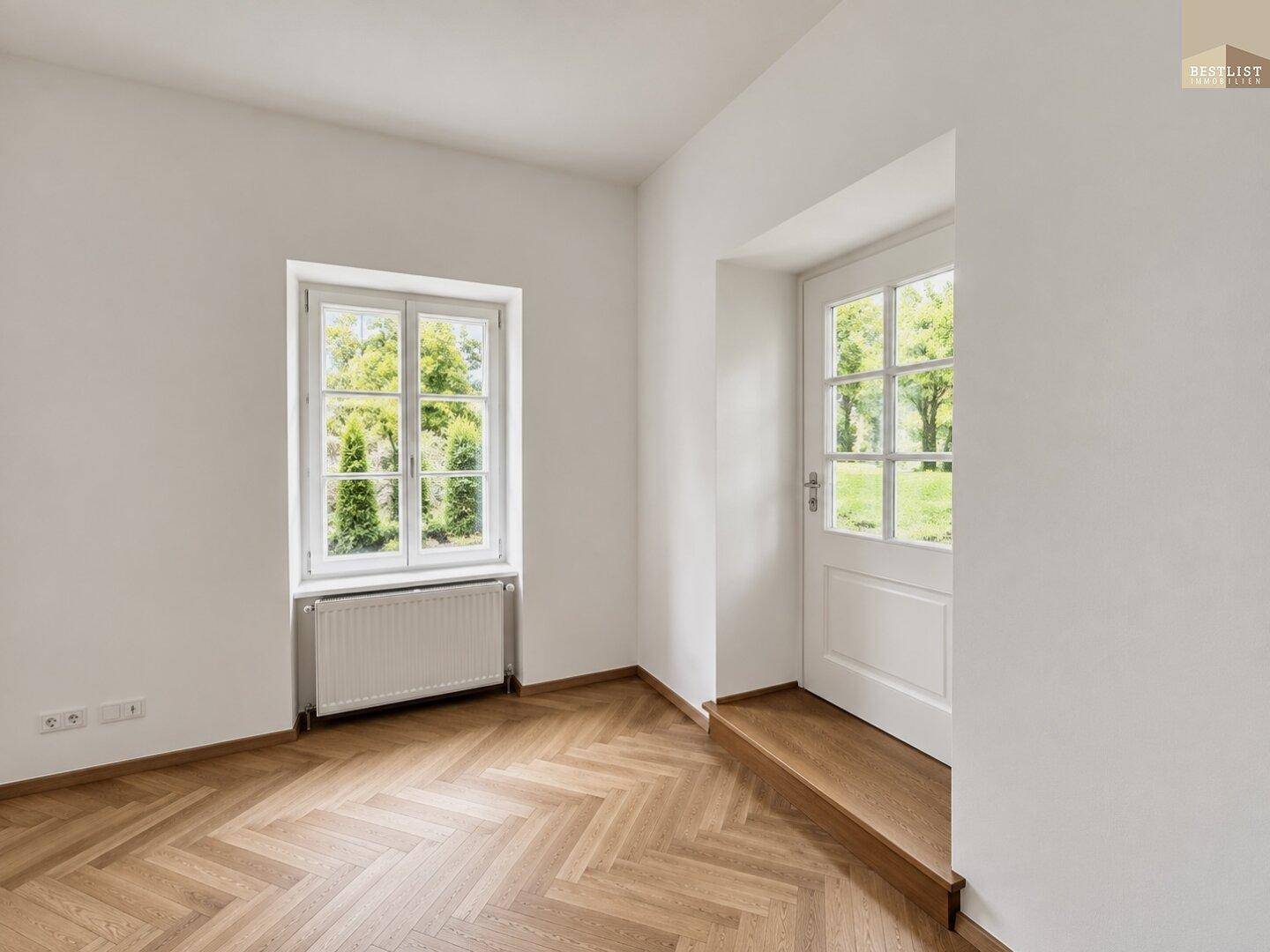 Heller Raum mit Fischgrätparkett, weißen Wänden und einem Fenster mit Blick ins Grüne.