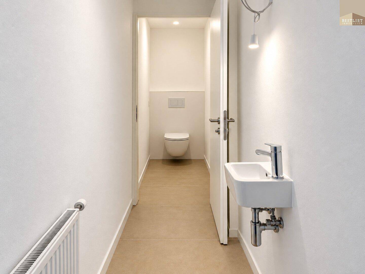 Schmaler Flur führt zu einer Gästetoilette mit wandhängendem WC und kleinem Waschbecken.