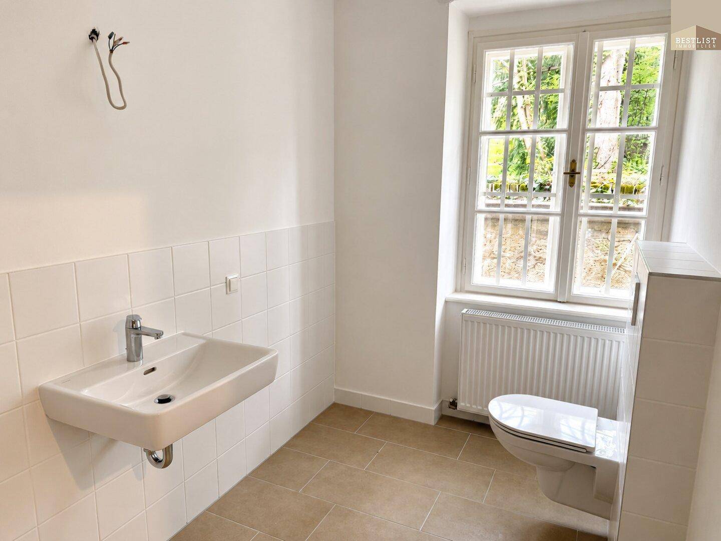 Helles Badezimmer mit Fenster, wandhängendem WC und modernem Waschbecken, gefliesten Wänden.