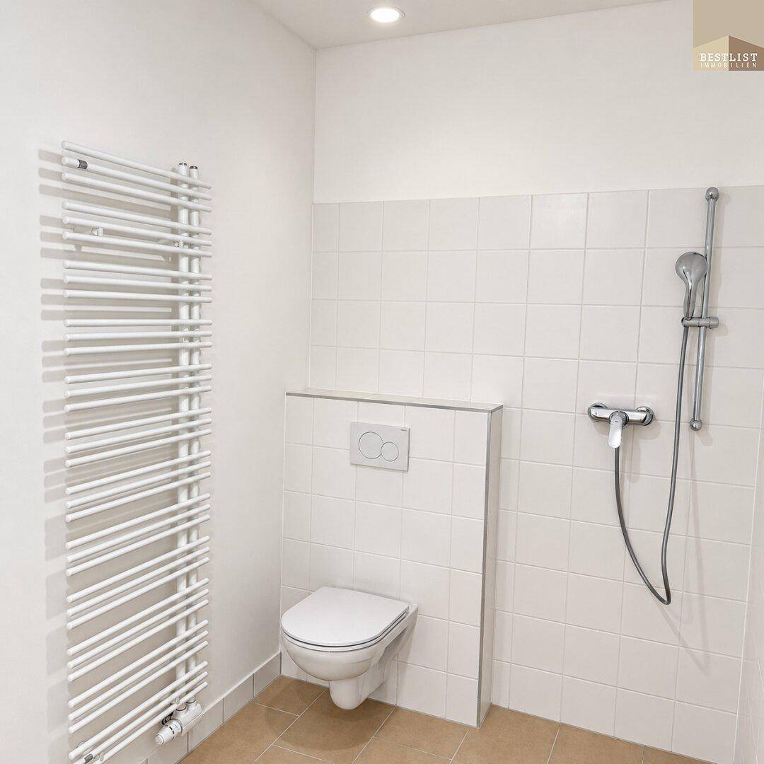 Modernes Badezimmer mit Duschbereich, wandhängendem WC und Handtuchheizkörper, hell gefliest.