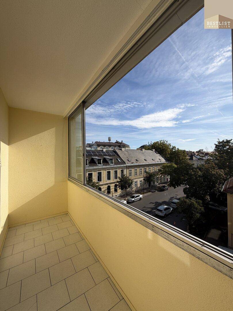 Sonniger Balkon mit Fliesenboden und weitem Blick über die Dächer der Stadt.