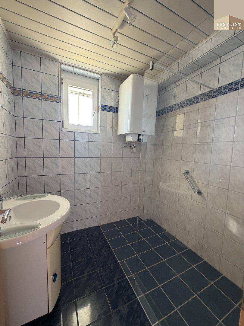 Gefliestes Badezimmer mit Waschbecken, Fenster und Haltegriffen für mehr Sicherheit.