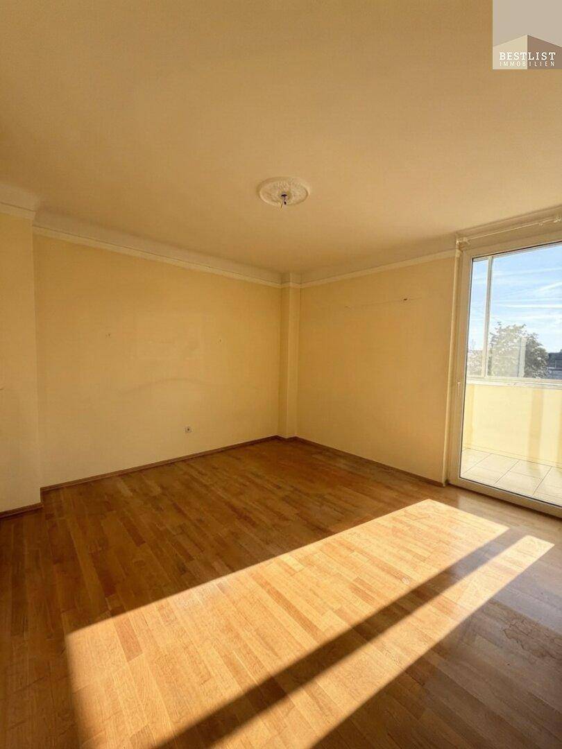 Helles Zimmer mit Holzboden und Zugang zu einem Balkon, durchflutet von Sonnenlicht.