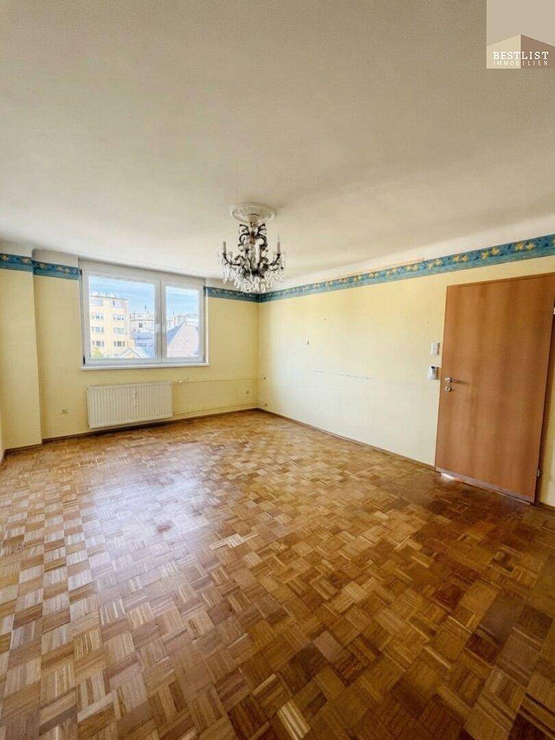 Geräumiges Wohnzimmer mit Parkettboden, großem Fenster und einem eleganten Kronleuchter.
