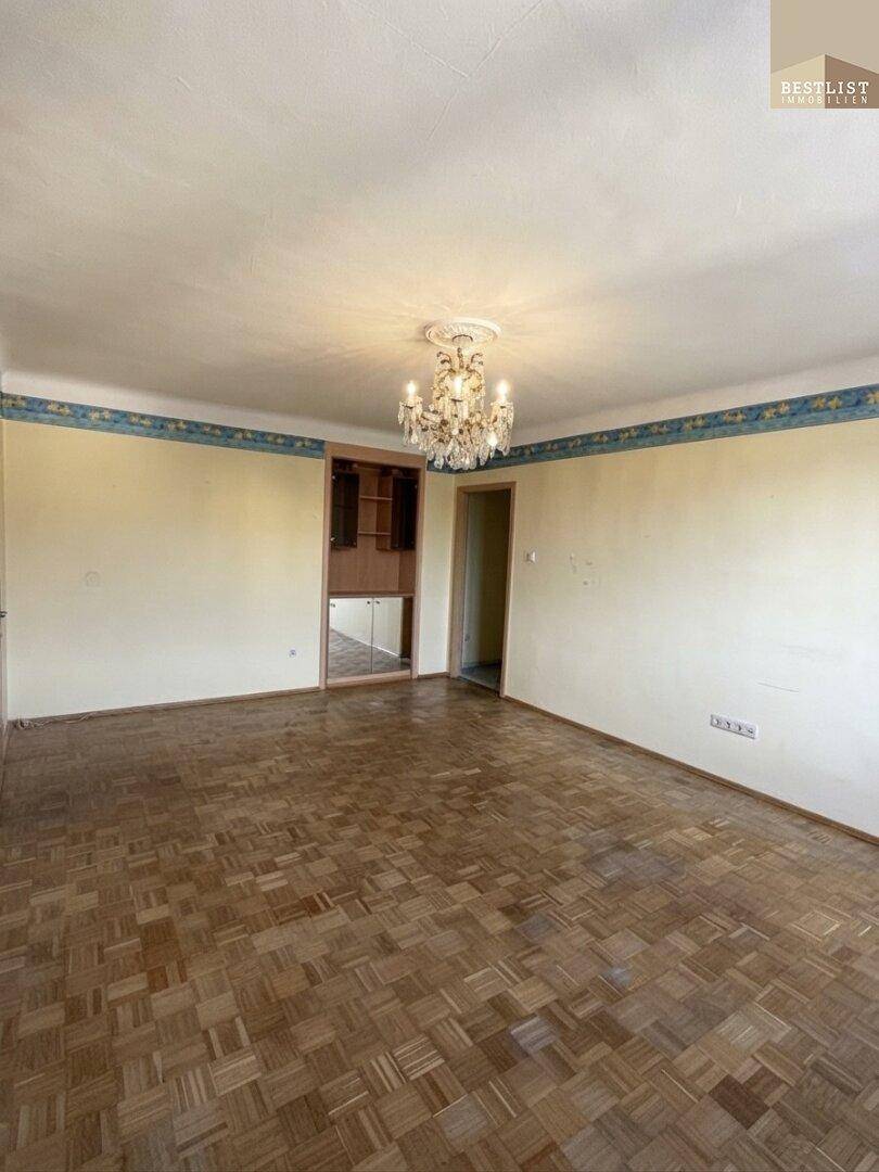 Wohnzimmer mit Parkettboden und integrierten Regalen, beleuchtet von einem Kronleuchter.