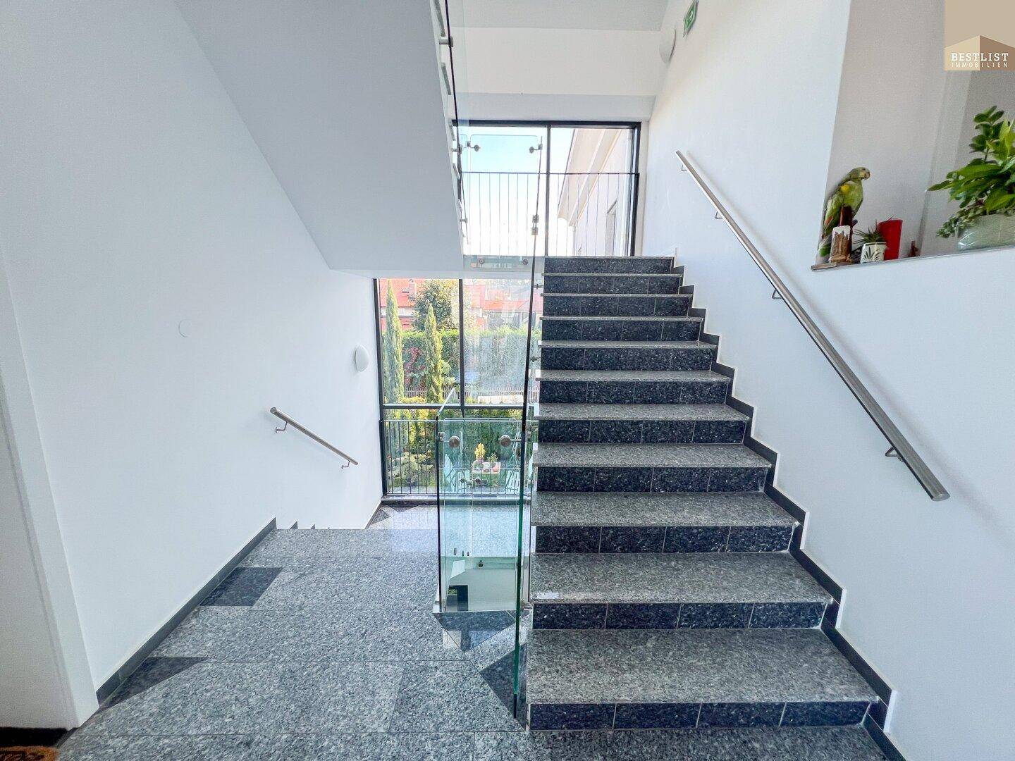 Modernes Treppenhaus mit Granitstufen, Glasgeländer und viel Tageslicht.