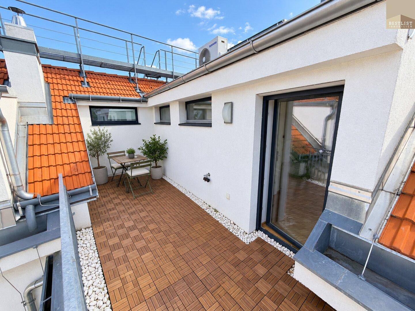 Gemütliche Dachterrasse mit Holzboden, Sitzgelegenheiten und Blick auf die Dächer.