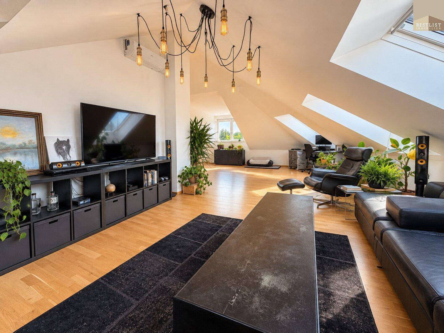 Geräumiges Wohnzimmer mit großem Fernseher, schwarzen Möbeln und viel Tageslicht durch Dachfenster.