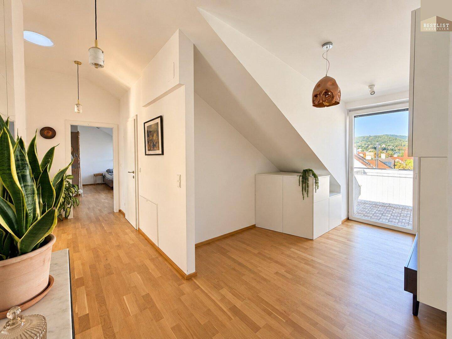 Heller Flur mit Holzboden, Dachschrägen und Zugang zu einem Außenbereich.