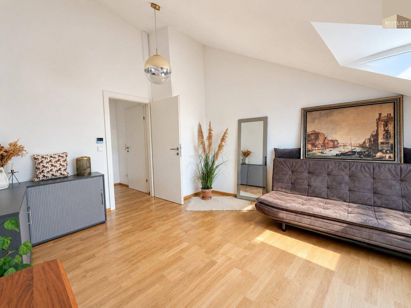 Helles Zimmer mit Holzboden, Schlafsofa und moderner Dekoration unter Dachschrägen.