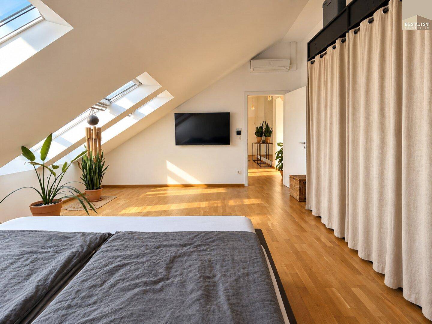 Schlafzimmer mit Doppelbett, Fernseher und viel Tageslicht durch die Dachfenster.