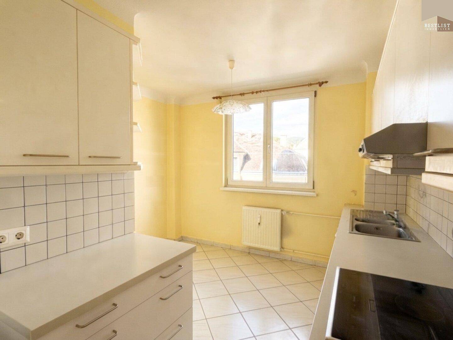 Helle Küche mit gelben Wänden, weißen Fliesen und einem Fenster, das Tageslicht hereinlässt.