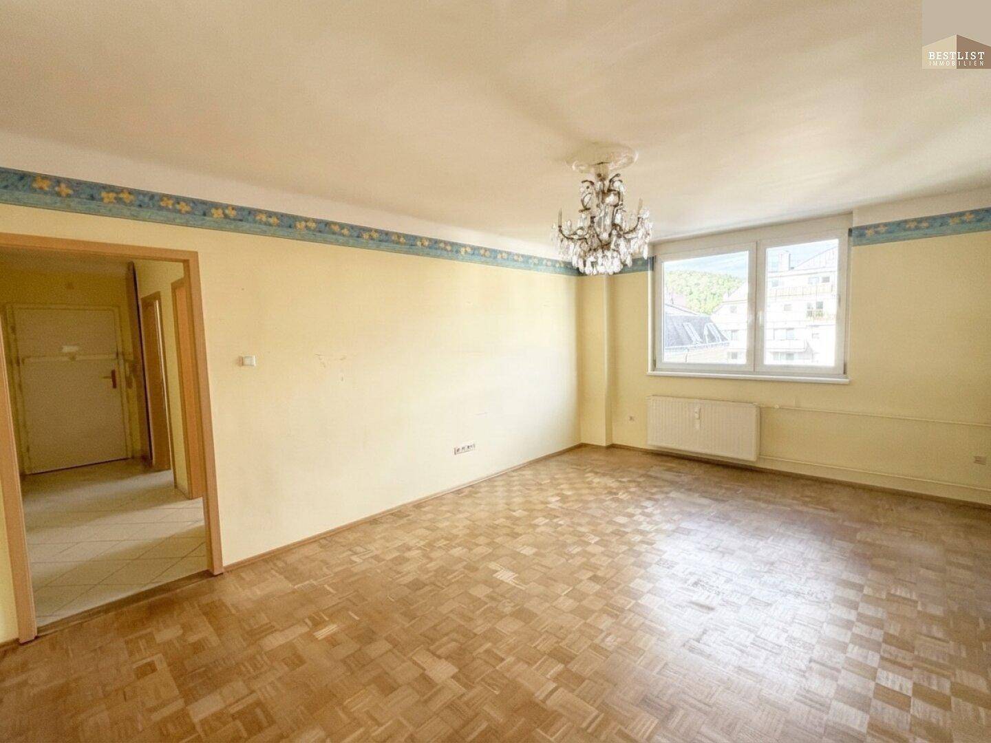 Helles Wohnzimmer mit Parkettboden, Kronleuchter und einem dekorativen Wandfries.