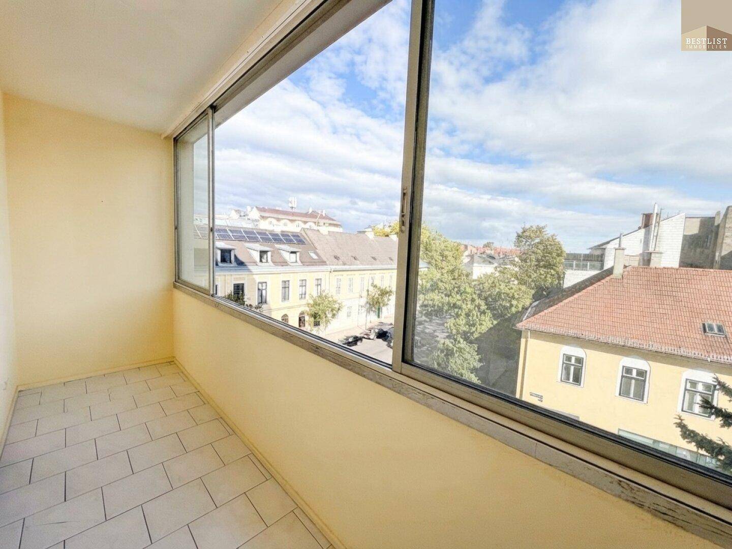 Verglaster Balkon mit Fliesenboden und weitem Blick über die städtische Umgebung.