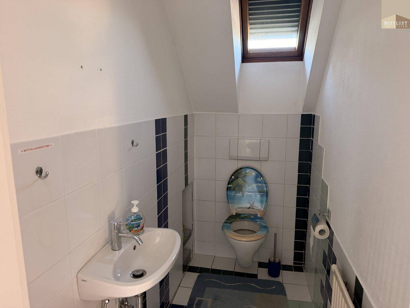 Kleines Gäste-WC mit Waschbecken, Toilette und Dachfenster, in einfachen Fliesen gehalten.
