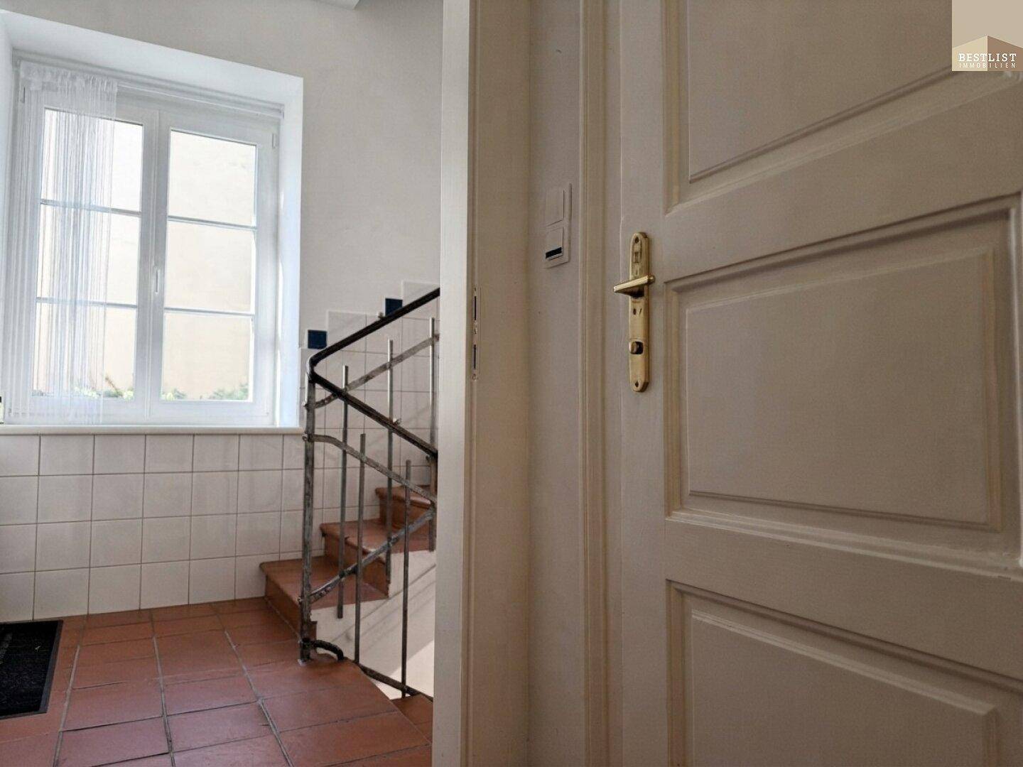Treppenhaus mit Terrakottafliesen und schmiedeeisernem Geländer, beleuchtet durch ein Fenster.