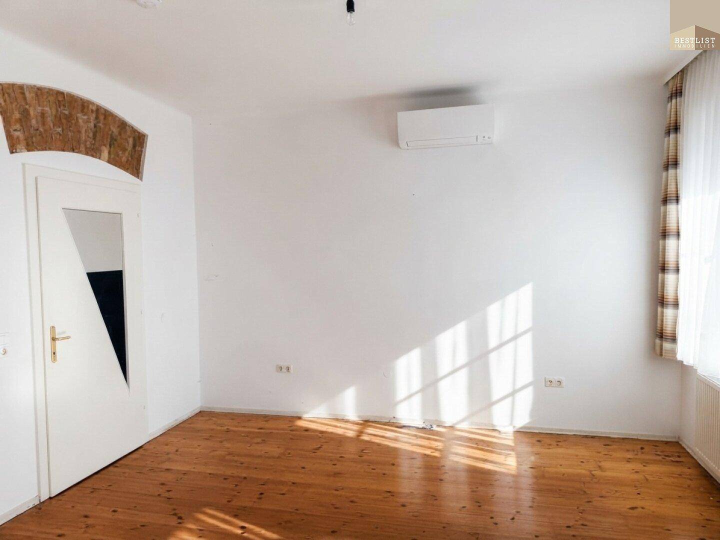 Leerer Wohnraum mit Holzboden, weiß gestrichenen Wänden und Klimaanlage.
