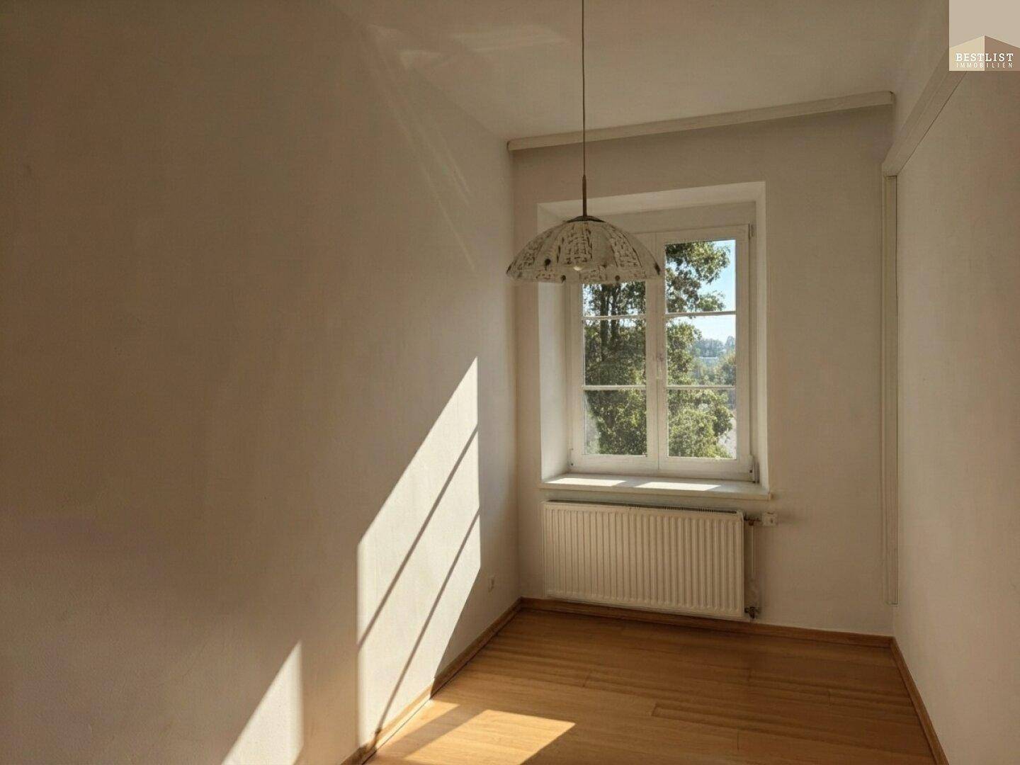Kleiner Raum mit Holzboden, Fenster und Heizkörper, ideal als Schlaf- oder Arbeitszimmer.