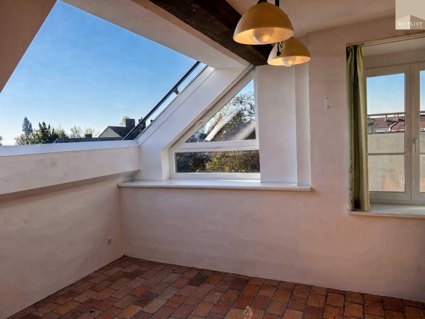 Dachgeschossraum mit schrägen Wänden, Dachfenstern und Terrakottaboden, bietet viel Tageslicht.