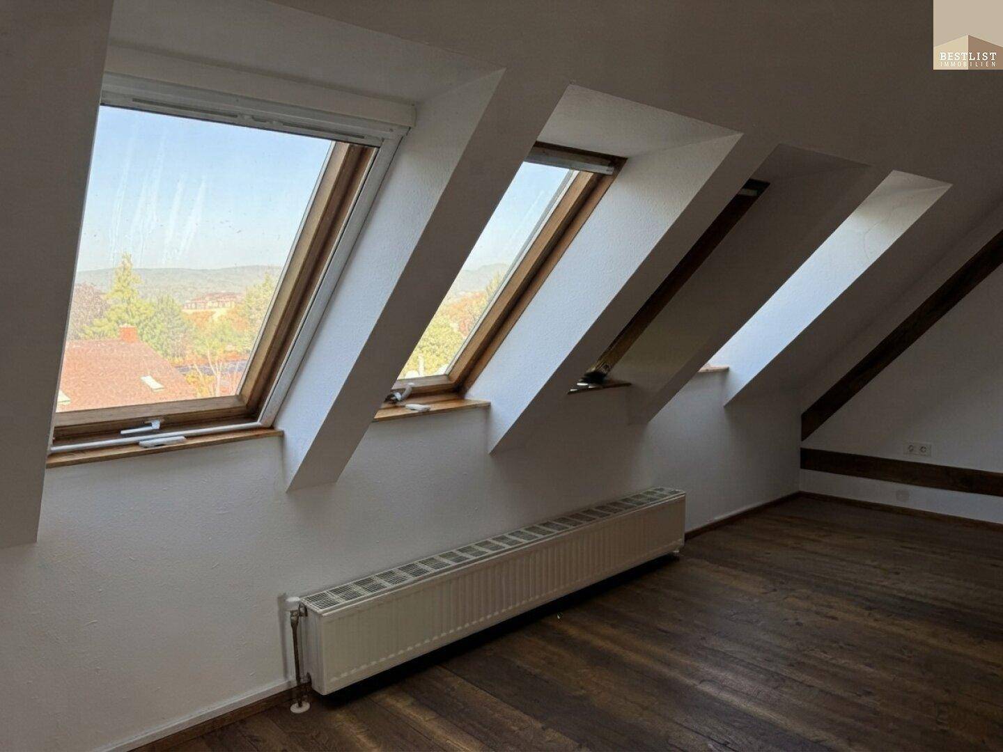 Dachgeschosszimmer mit Holzboden, schrägen Wänden und mehreren Dachfenstern für viel Licht.