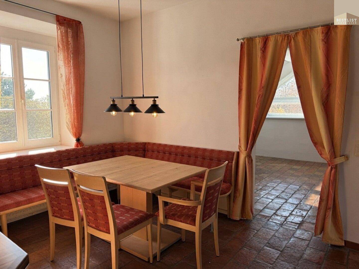 Gemütlicher Essbereich mit Eckbank, Holztisch und Vorhängen, angrenzend an einen weiteren Raum.