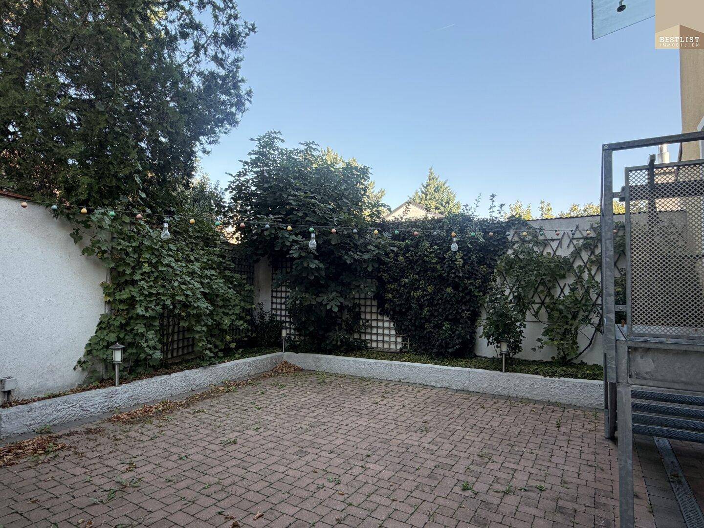 Gepflasterte Terrasse mit Lichterkette und Rankgittern, ideal für gemütliche Abende im Freien.