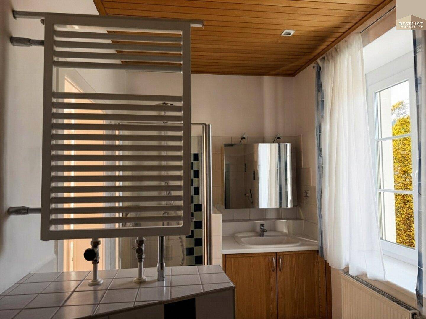 Badezimmer mit Holzdecke, Waschbecken, Spiegelschrank und beheiztem Handtuchhalter.