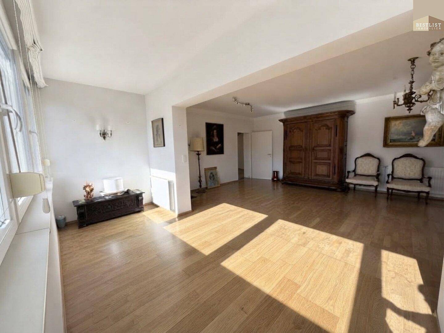 Weitläufiges Wohnzimmer mit hellem Parkettboden und traditionellen Möbeln, durchflutet von Tageslicht.