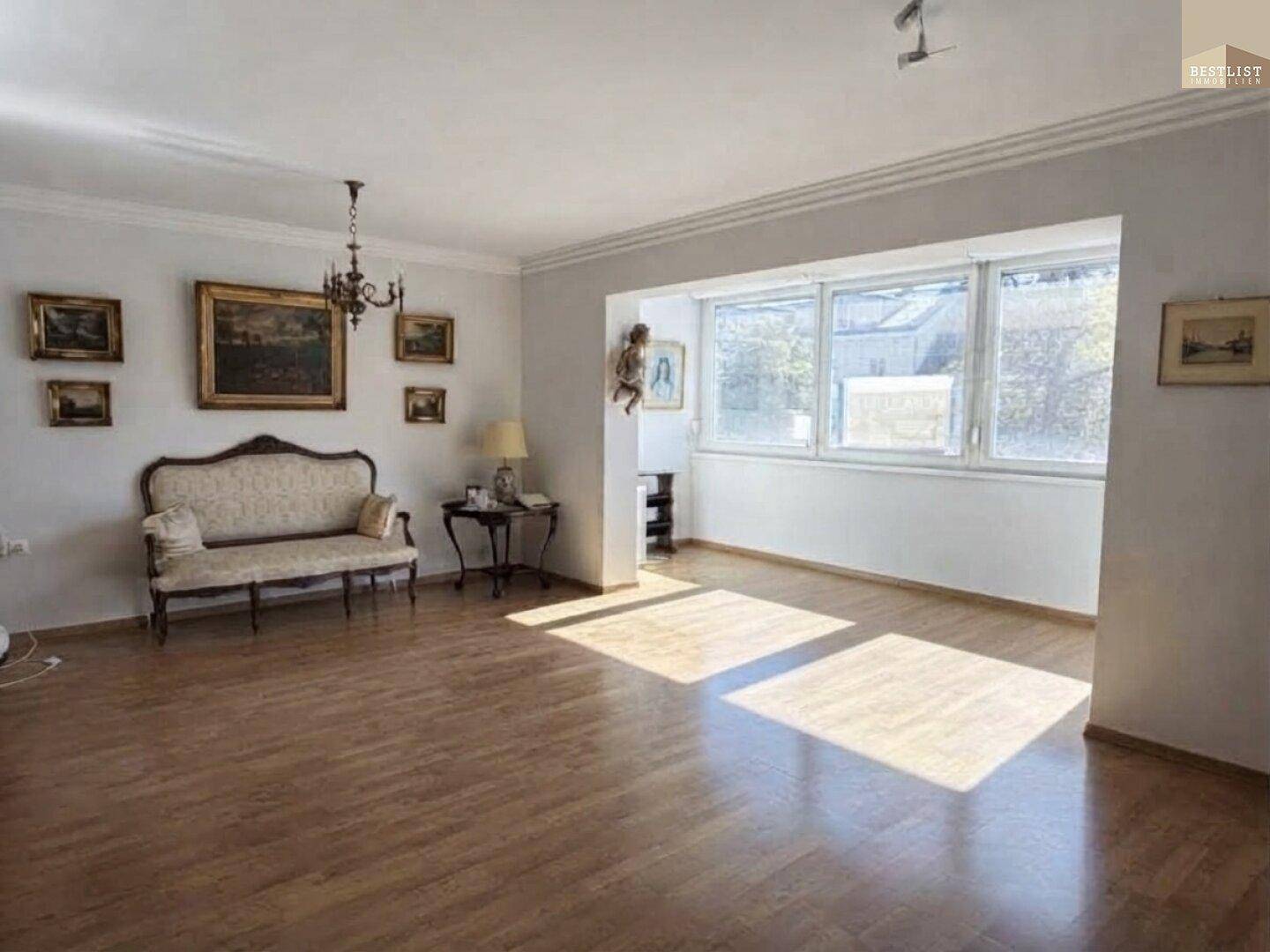 Geräumiges Wohnzimmer mit Parkettboden, Stuckelementen und großen Fenstern, die viel Licht hereinlassen.