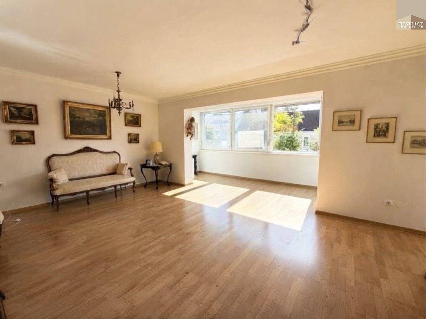 Helles Wohnzimmer mit klassischem Parkettboden und großen Fenstern, die eine angenehme Atmosphäre schaffen.