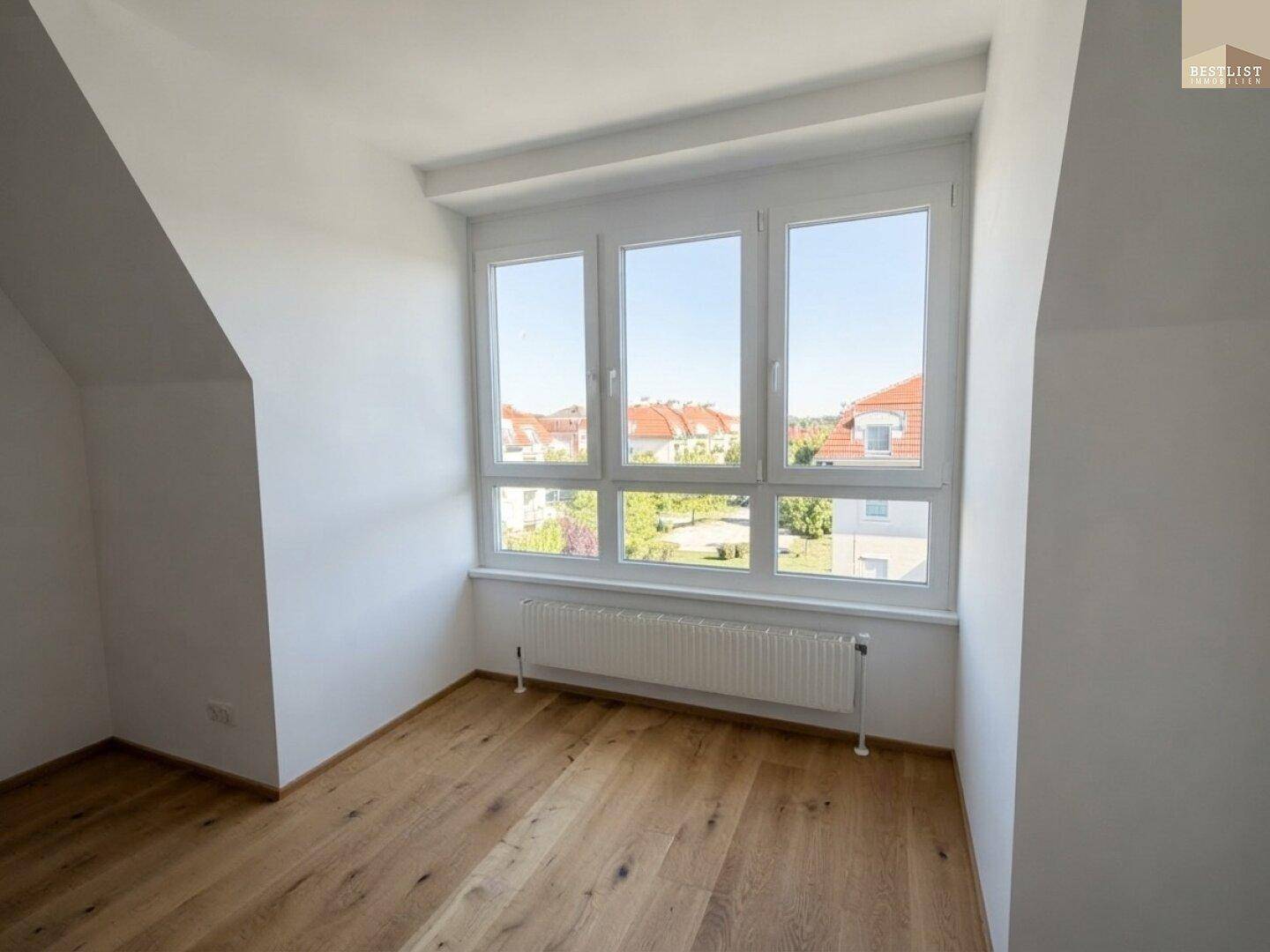 Lichtdurchflutetes Zimmer mit Holzboden und Ausblick ins Grüne, perfekt für ein Schlafzimmer.