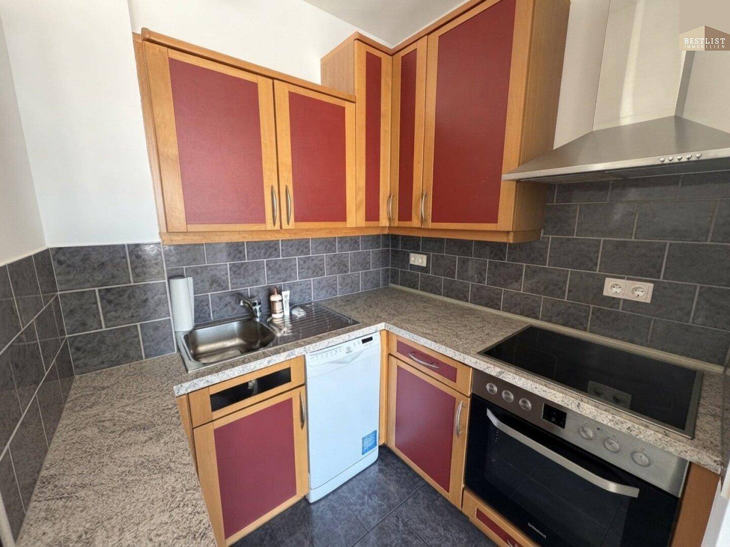 Funktionale Küche mit roten und holzfarbenen Schränken, ausgestattet mit modernen Geräten.