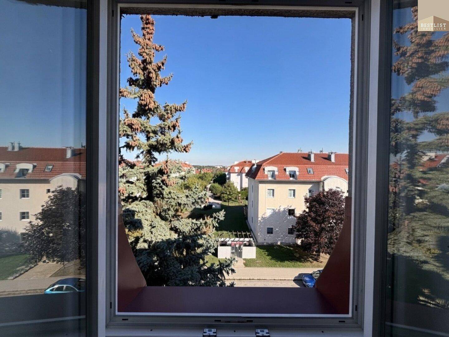 Ausblick aus dem Fenster auf die umliegende Wohngegend mit Bäumen und Häusern.