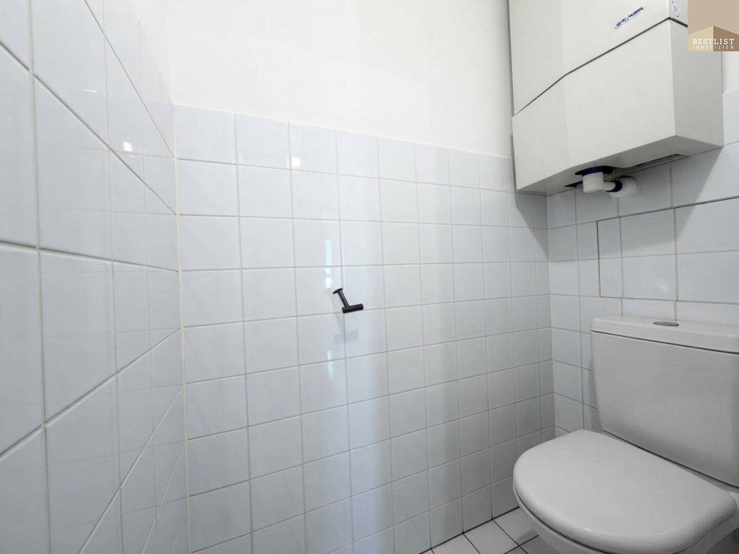 Kleines WC mit weißen Fliesen und Toilette, ausgestattet mit einem Warmwasserboiler.