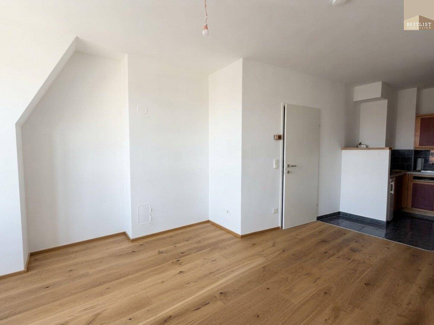 Offener Wohnbereich mit Holzboden und Dachschrägen, angrenzend an die Küche.