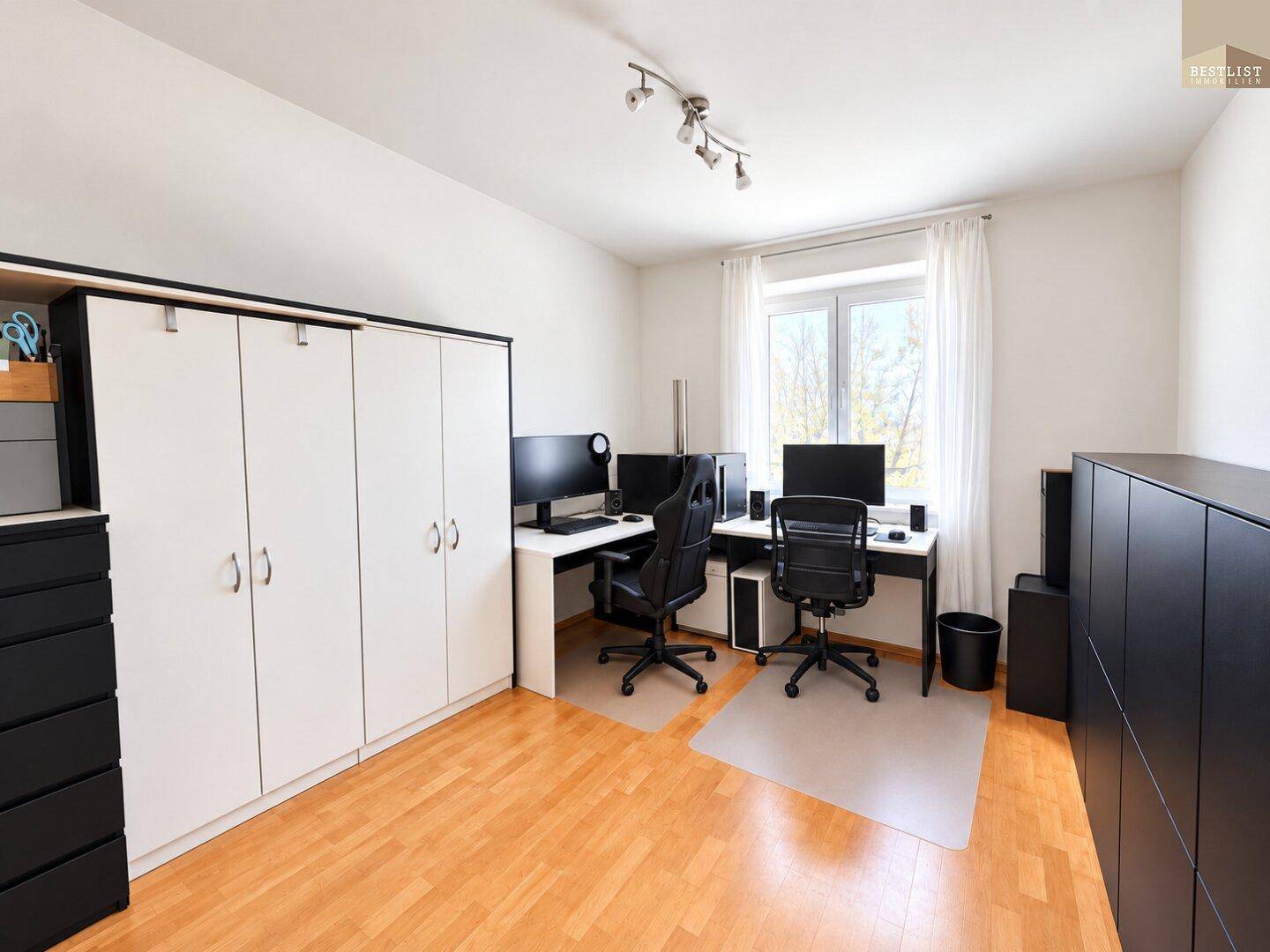 Geräumiges Arbeitszimmer mit Holzboden, Einbauschränken und zwei modernen Arbeitsplätzen.