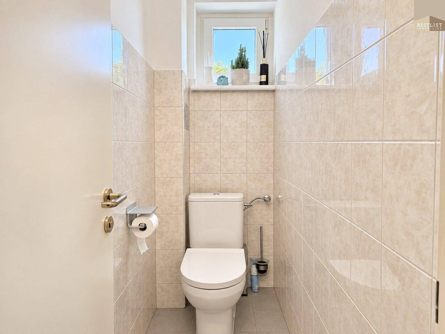 Kleines Gäste-WC mit Fenster, hellen Wandfliesen und einer modernen Toilette.