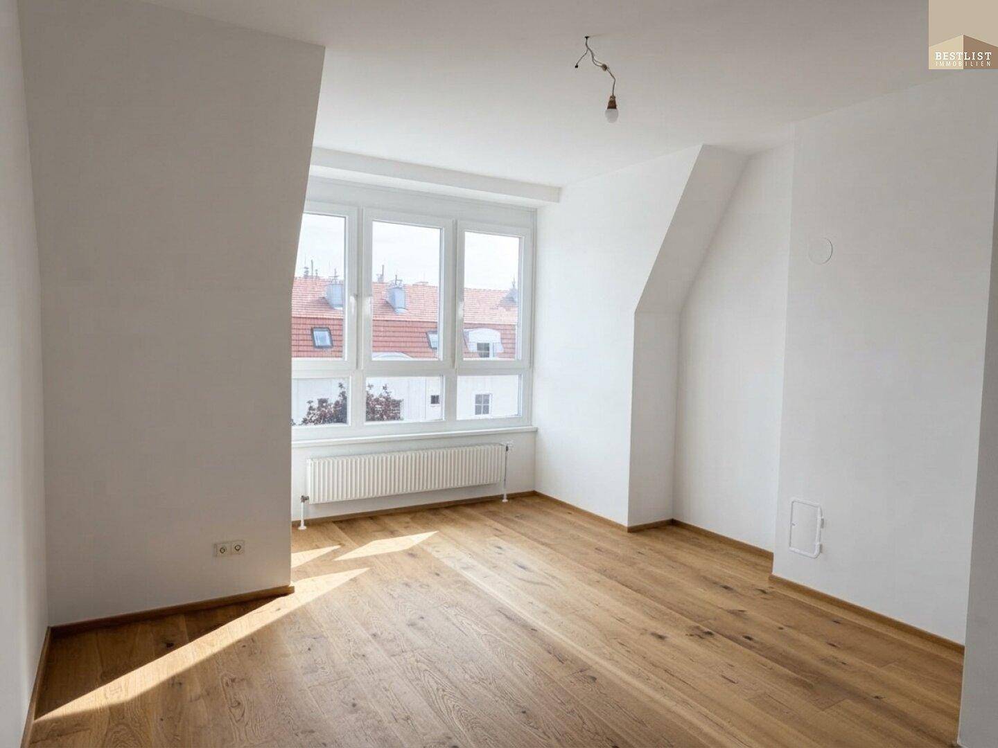 Geräumiges Zimmer mit viel Tageslicht, Holzboden und charakteristischen Dachschrägen.