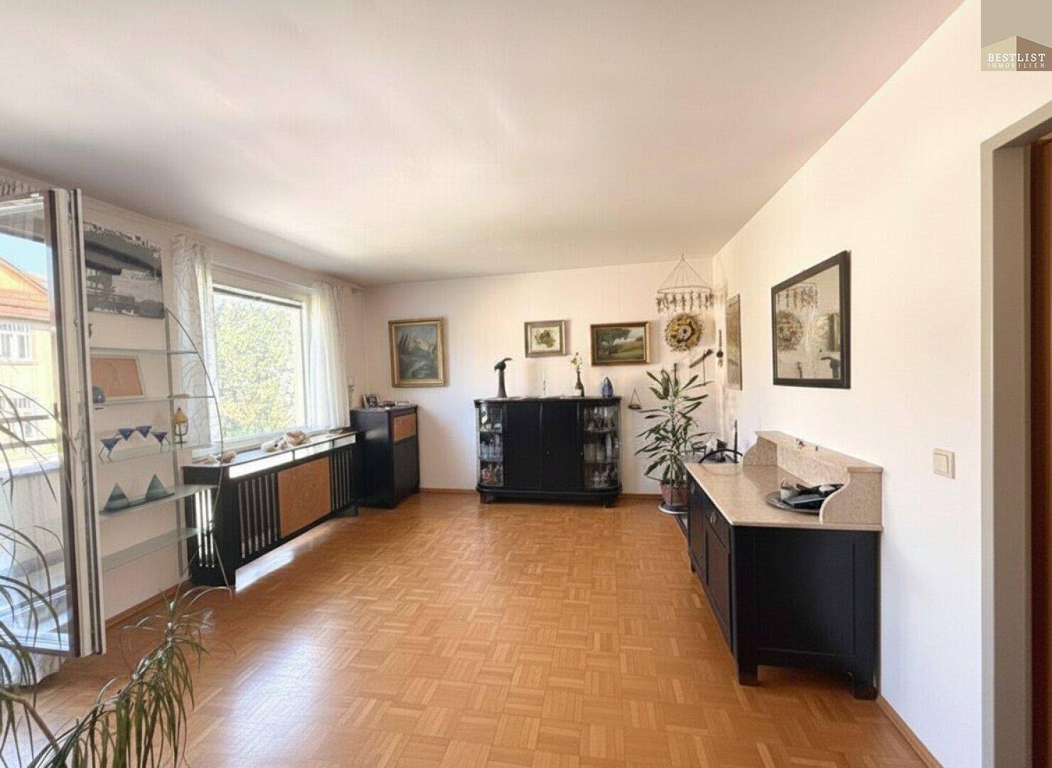Helles Wohnzimmer mit Parkettboden, großen Fenstern und klassischem Mobiliar sowie Balkonzugang.