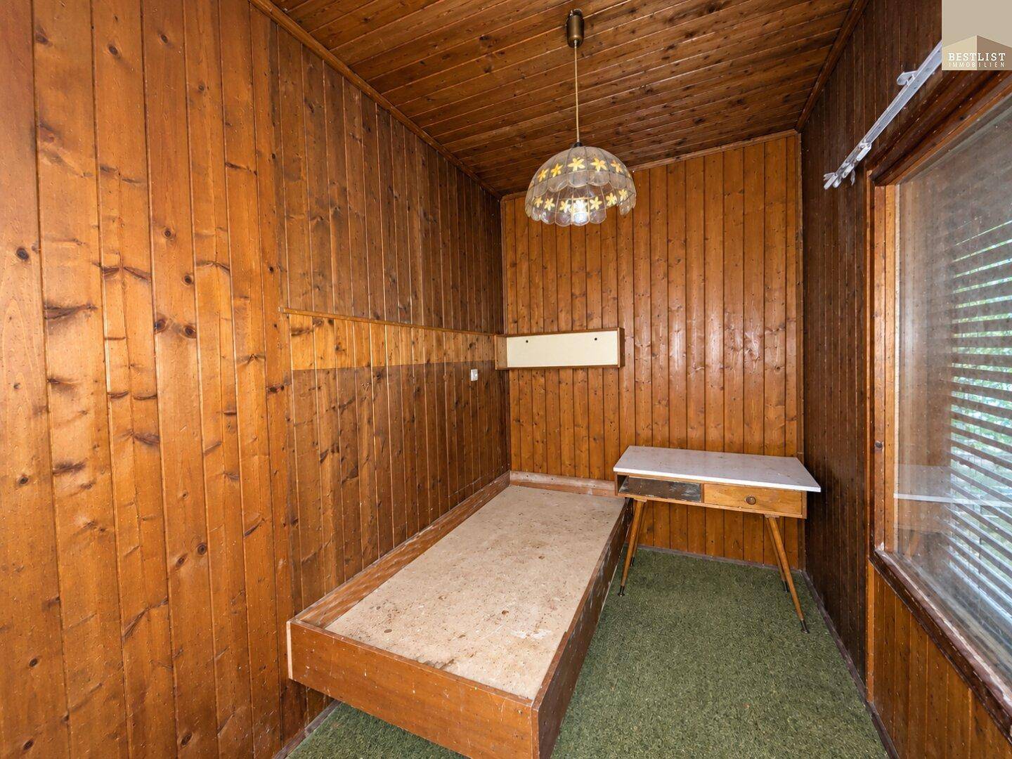 Schlafzimmer mit Holzvertäfelung, einem einfachen Einzelbett und grünem Teppichboden.