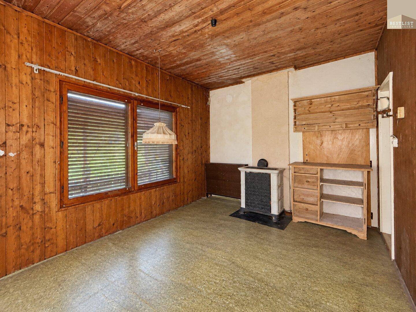 Rustikales Zimmer mit Holzvertäfelung, Linoleumboden und einem kleinen Kaminofen.