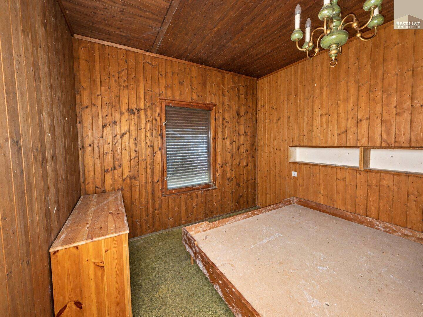 Schlafzimmer mit Holzvertäfelung, einem Doppelbett und grünem Teppichboden.