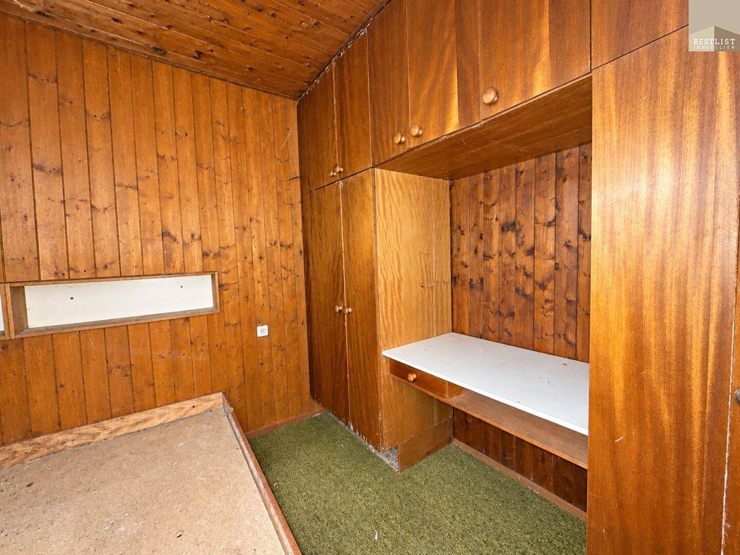 Schlafzimmer mit Holzvertäfelung, integrierten Schränken und grünem Teppichboden.
