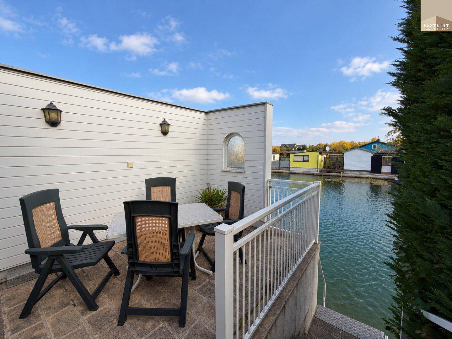 Gemütliche Terrasse mit Gartenmöbeln direkt am Wasser unter blauem Himmel, perfekt zum Entspannen.