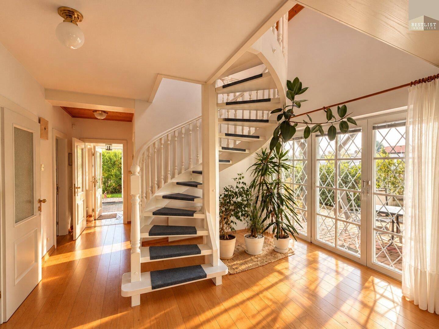 Geräumiger Flur mit Wendeltreppe, Holzboden und viel Tageslicht durch große Fenster zum Garten.