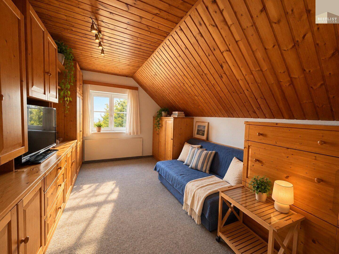 Helles Zimmer im Dachgeschoss mit Holzdecke, Sofa und viel Stauraum durch eingebaute Schränke.