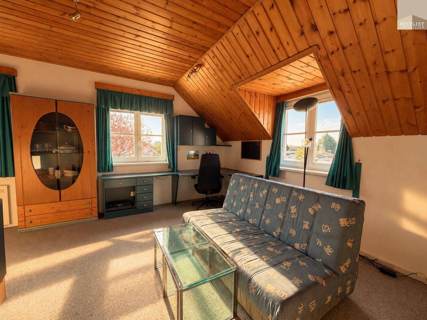 Wohnzimmer im Dachgeschoss mit Holzdecke, Sofa und Schreibtischbereich, ideal für Arbeit und Entspannung.