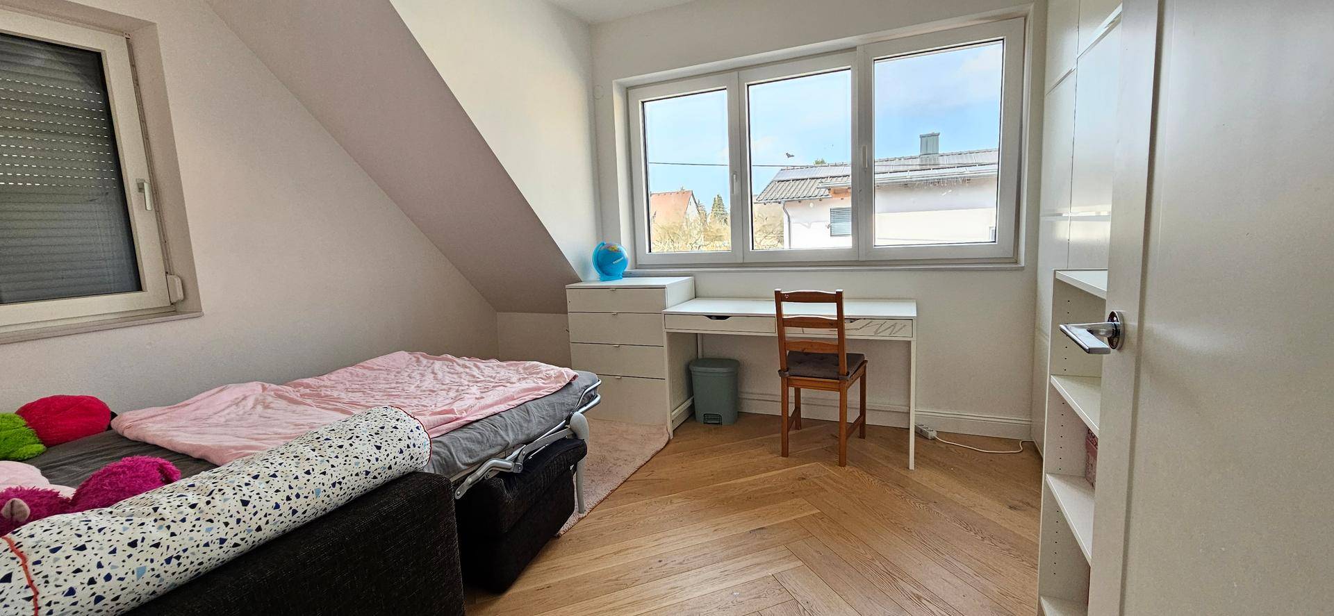 Weiteres Kinderzimmer mit Schreibtisch, Dachschräge und hellem Fischgrätparkettboden.